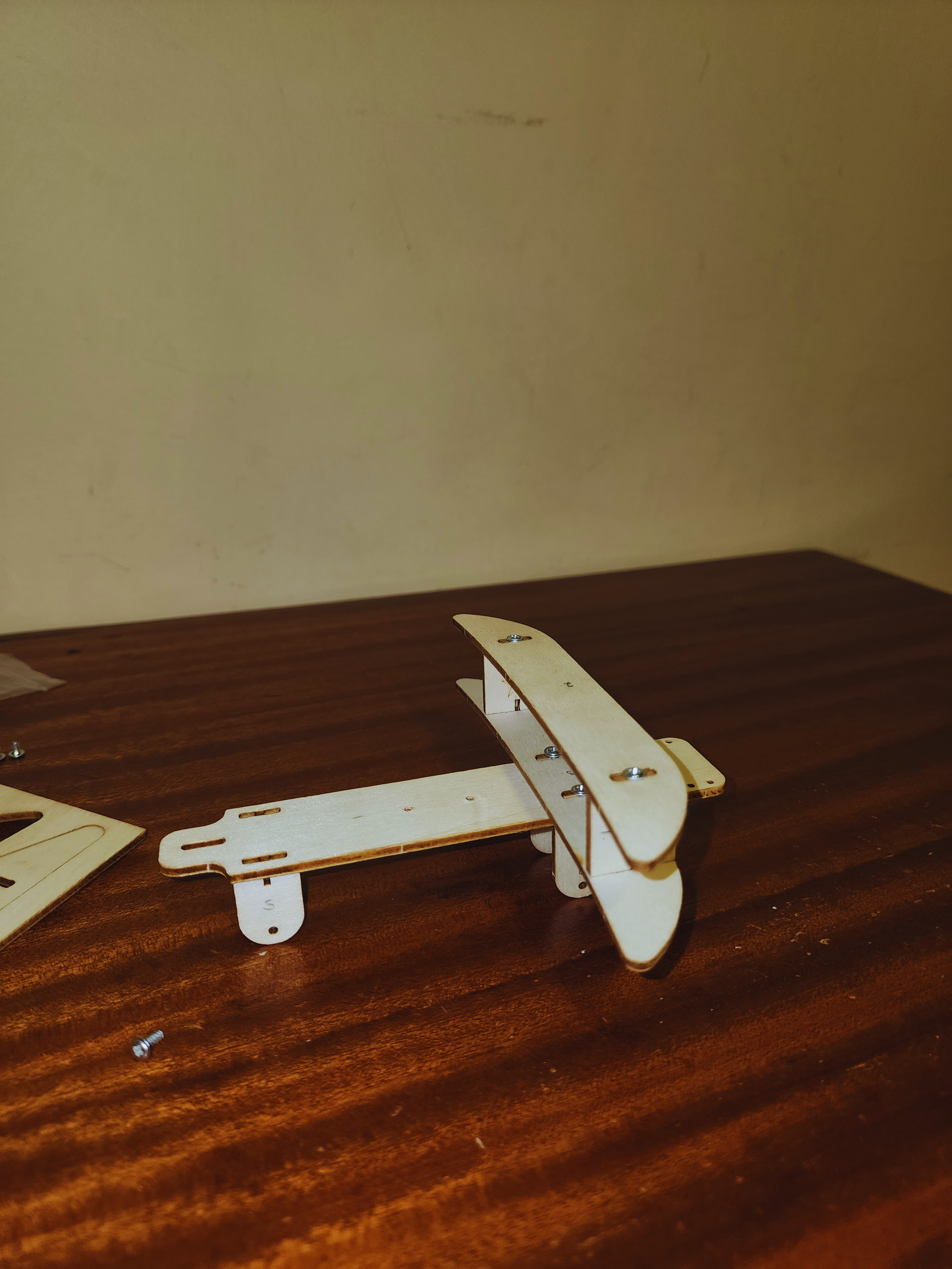 Beginner biplane engineering kit in progress with wooden wings secured by screws during the structural assembly stage.